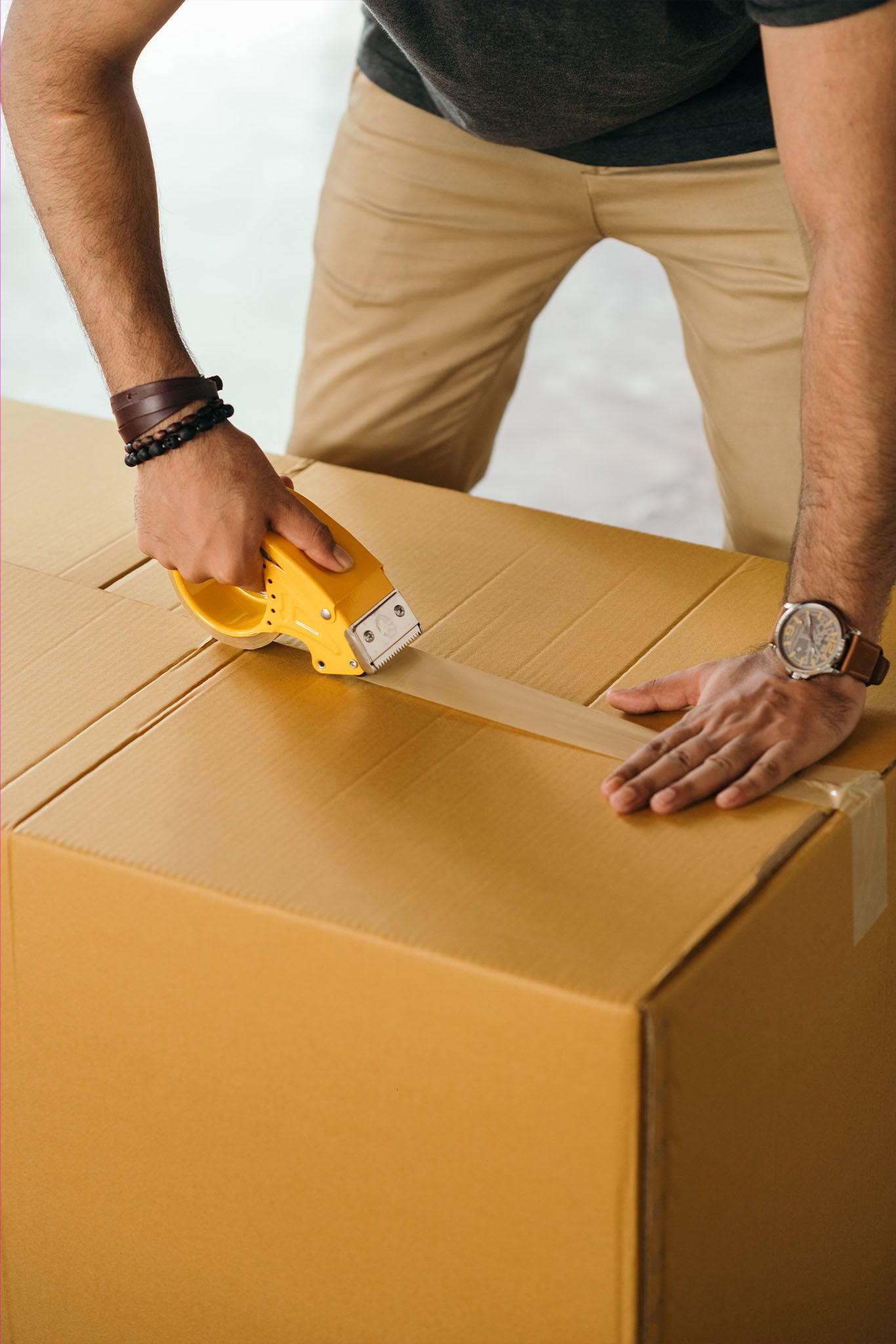 A man is packing and taping a box with clothes from a clothing brand to fulfill an order